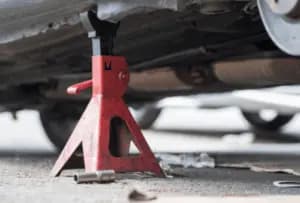 Red jack stand placed under a vehicle to hold it up. 